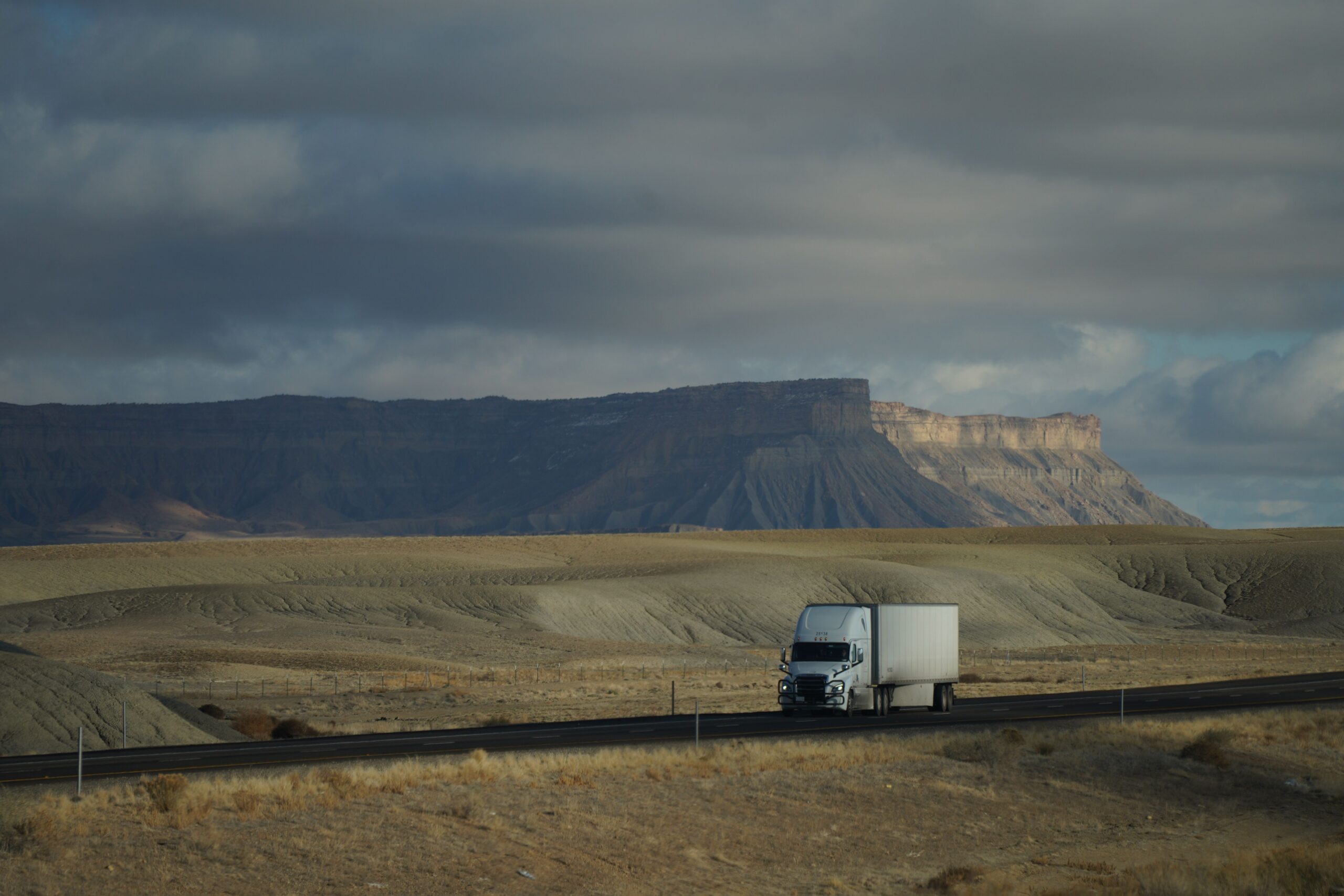 Semi-truck driving through desert landscape under dramatic cloudy sky