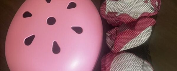 Recalled pink 5Color children's bicycle helmet with ventilation slots, shown with pink and white knee and elbow pads in a mesh bag