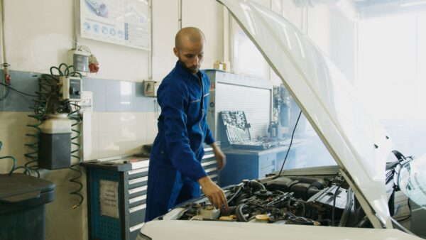 Mechanic inspecting a car engine in an auto repair shop. Photo credit: Pexels.