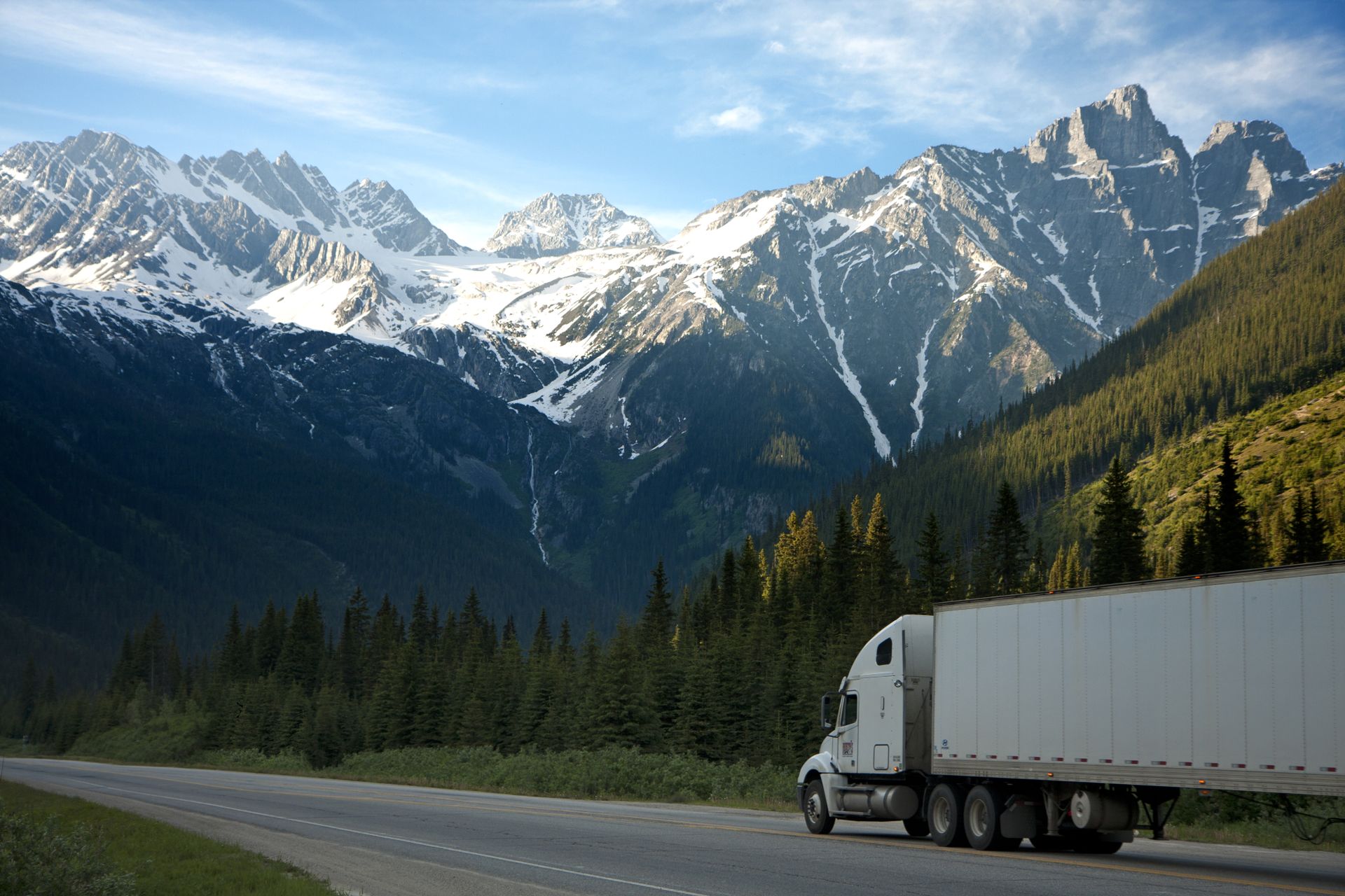 Semi truck driving on a highway with snow-capped mountains in the background. Photo credit: Pexels.